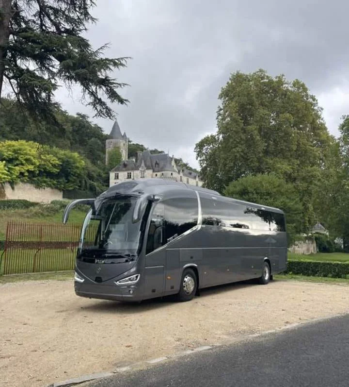 Autocar gris de grand tourisme avec chauffeur garé devant un château, pour les voyages de groupe
