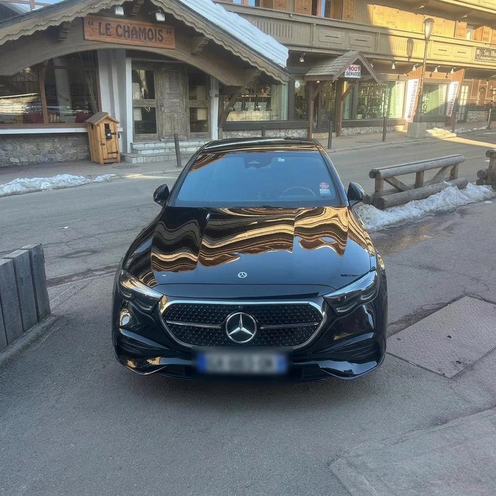 Mercedes-Benz Classe E noire avec chauffeur privé devant un chalet de montagne